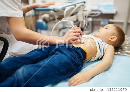 Boy undergoing thyroid ultrasound examination. Doctor examining kid throat in clinic with equipment. 135211970
