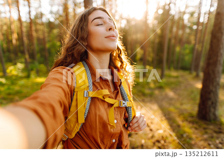Beautiful woman taking picture of herself while walking in sunny forest. Selfie in nature. Adventure Beautiful woman taking picture of herself while walking in sunny forest. Selfie in nature. Adventure 135212611