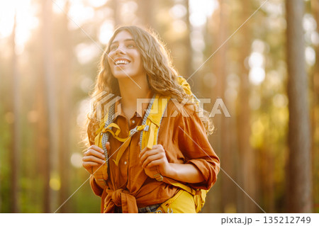 Tourist woman hiking alone in thick autumn forest. Stylish female looks for pathway among trees. 135212749