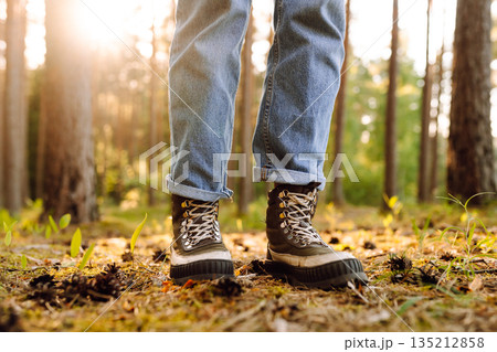 Hiker's boots stepping on a blanket of fallen autumnal orange leaves in the forest. Travel 135212858