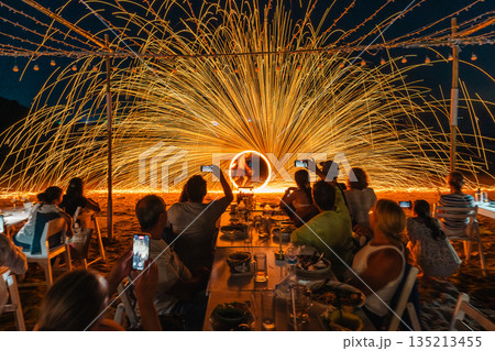 Tourists watch and record a spectacular fire spinning performance on the beach during a night event at Koh Samet, Rayong, Thailand 135213455