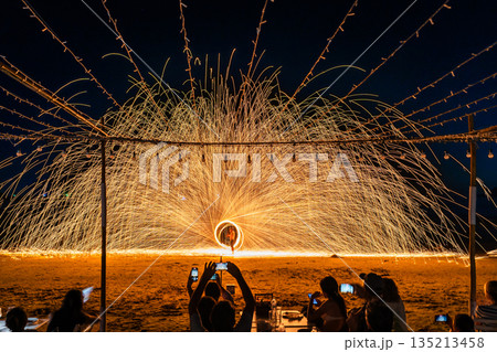 Tourists watch and record a spectacular fire spinning performance on the beach during a night event at Koh Samet, Rayong, Thailand Tourists watch and record a spectacular fire spinning performance on the beach during a night event at Koh Samet, Rayong, Thailand 135213458