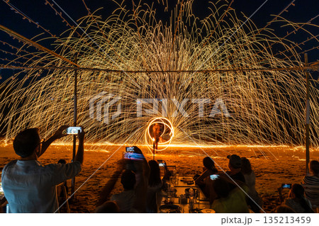 Tourists watch and record a spectacular fire spinning performance on the beach during a night event at Koh Samet, Rayong, Thailand Tourists watch and record a spectacular fire spinning performance on the beach during a night event at Koh Samet, Rayong, Thailand 135213459