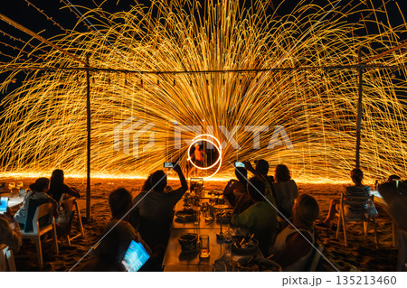 Tourists watch and record a spectacular fire spinning performance on the beach during a night event at Koh Samet, Rayong, Thailand 135213460