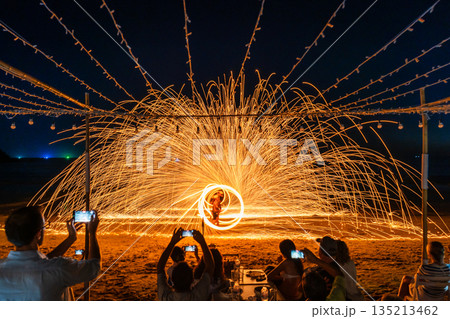 Tourists watch and record a spectacular fire spinning performance on the beach during a night event at Koh Samet, Rayong, Thailand Tourists watch and record a spectacular fire spinning performance on the beach during a night event at Koh Samet, Rayong, Thailand 135213462