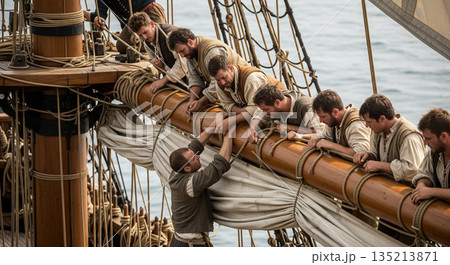 Two sailors grip a thick rope to pull and tighten the sail on a galleon as others assist from the rigging. The sea is calm and clear under the bright sky. 135213871