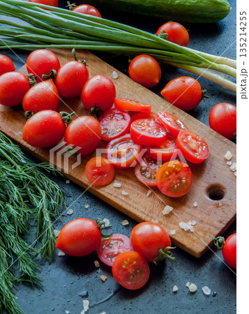 Fresh red cherry tomatoes with herbs and leek sprinkled with sea salt on wooden board on table, top view of vegetables covered with drops. Fresh red cherry tomatoes with herbs and leek sprinkled with sea salt on wooden board on table, top view of vegetables covered with drops. 135214255