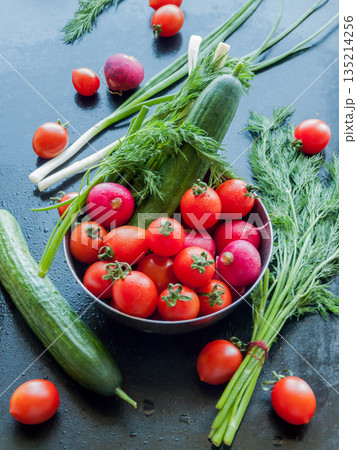 Bowl of fresh red cherry tomatoes, herbs, cucumber and radish on table background, close up vegetables in bowl covered with water drops. Bowl of fresh red cherry tomatoes, herbs, cucumber and radish on table background, close up vegetables in bowl covered with water drops. 135214256