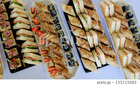 Gourmet catering featuring elegant platters with colorful canapes, triangular sandwiches, and delicate rolled crepes for professional event dining Gourmet catering featuring elegant platters with colorful canapes, triangular sandwiches, and delicate rolled crepes for professional event dining 135215083