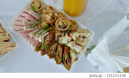 Rustic bakery selection featuring savory pies, ham cheese rolls, vegetable wraps, golden toasted sandwiches plated on crisp white surface with fresh orange juice Rustic bakery selection featuring savory pies, ham cheese rolls, vegetable wraps, golden toasted sandwiches plated on crisp white surface with fresh orange juice 135215136