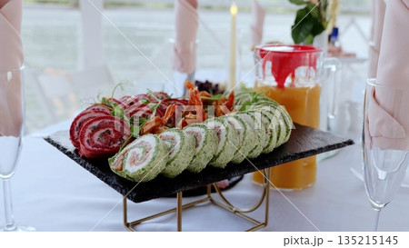 Gourmet catering display featuring spinach, beet, cream cheese rolls with shrimp on slate plate, paired with champagne and orange juice Gourmet catering display featuring spinach, beet, cream cheese rolls with shrimp on slate plate, paired with champagne and orange juice 135215145