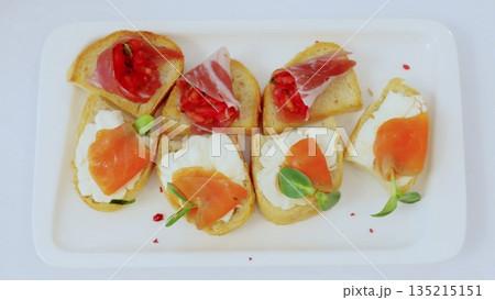 Appetizing bruschetta featuring smoked salmon, cream cheese, cured ham, diced tomatoes, garnished with fresh herbs on crisp toasted bread slices 135215151