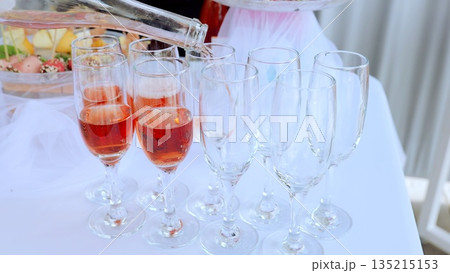 Sommelier serving chilled rose wine into crystal glasses near gourmet appetizer platter, highlighting luxurious dining experience on crisp white tablecloth Sommelier serving chilled rose wine into crystal glasses near gourmet appetizer platter, highlighting luxurious dining experience on crisp white tablecloth 135215153