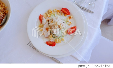 Crisp romaine lettuce tossed with grilled chicken, golden croutons, shaved parmesan, ripe cherry tomatoes resting on pristine white linen, embodying classic caesar salad elegance Crisp romaine lettuce tossed with grilled chicken, golden croutons, shaved parmesan, ripe cherry tomatoes resting on pristine white linen, embodying classic caesar salad elegance 135215168