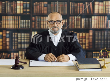 Judge in robe sitting at brown desk with gavel and balance scales, law books 135215442