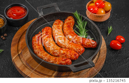 Grilled sausages in cast iron pan with rosemary and cherry tomatoes on dark background 135216745