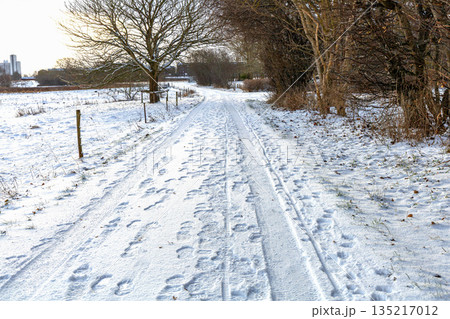 Snowy village road with car and foot tracks 135217012