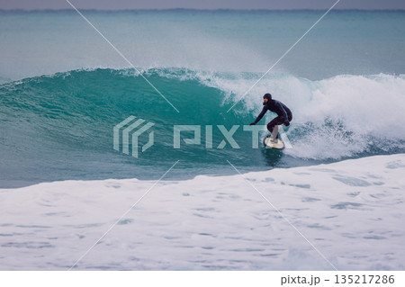 Surfer in wetsuit rides on wave in ocean. Winter surfing on perfect waves Surfer in wetsuit rides on wave in ocean. Winter surfing on perfect waves 135217286