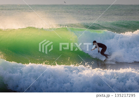 Surfer male ride on wave in cold winter ocean with evening sun light Surfer male ride on wave in cold winter ocean with evening sun light 135217295