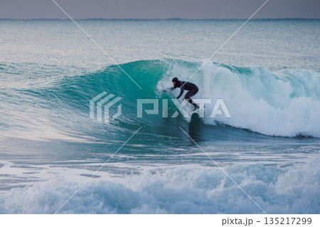Surfer in winter wetsuit ride the blue waves in ocean. Surfer in winter wetsuit ride the blue waves in ocean. 135217299