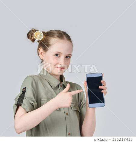Young caucasian female child pointing at smartphone screen with confident smile Young caucasian female child pointing at smartphone screen with confident smile 135217413