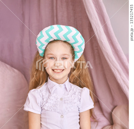 Smiling caucasian young girl with pigtails wearing chevron hat in pink room 135217455