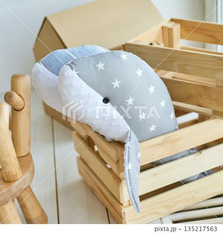 Cozy gray and white plush whale with stars in wooden crate on light wooden Cozy gray and white plush whale with stars in wooden crate on light wooden 135217563