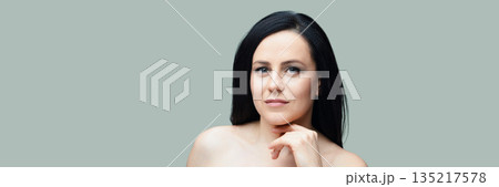 Confident young caucasian female with long black hair against a grey background 135217578