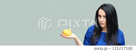 Young caucasian female holding yellow piggy bank against plain background Young caucasian female holding yellow piggy bank against plain background 135217580