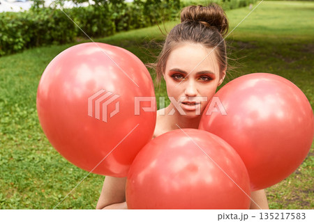Young caucasian female with red balloons in park setting 135217583