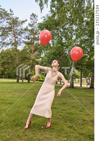 Young caucasian female in white dress with red balloons in park surrounded 135217584