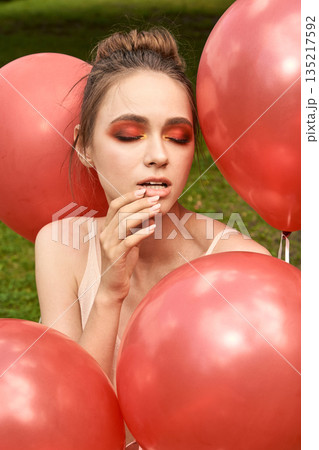 Young caucasian female with red eye makeup posing with pink balloons outdoors 135217592