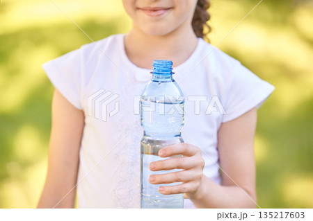 Young caucasian girl holding open water bottle outdoors on a sunny day 135217603