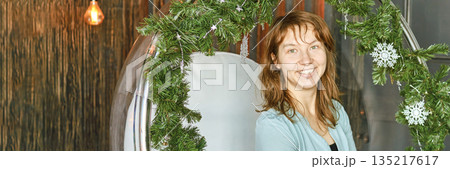 Caucasian young adult female smiling near holiday wreath with hanging light Caucasian young adult female smiling near holiday wreath with hanging light 135217617