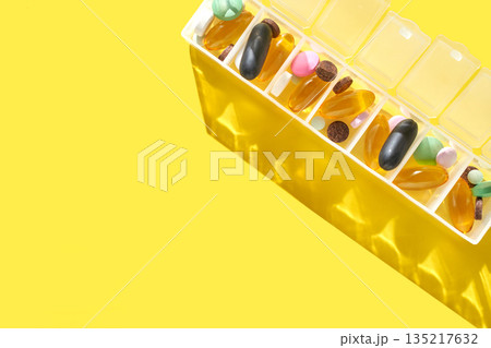 Colorful weekly pill organizer with various vitamins and supplements on bright 135217632