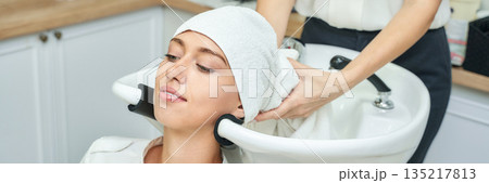 Young caucasian female enjoying hair wash at salon with towel wrapped head 135217813