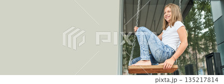 Caucasian young girl in casual outfit enjoying a swing in a modern outdoor 135217814