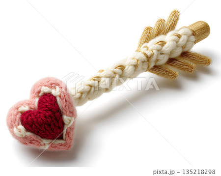 Knitted Cupid's arrow with pink heart and gold accents on white background 135218298