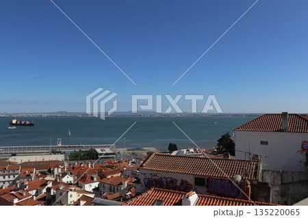 Panoramic view of Alfama rooftops and the Tagus River estuary with a cargo ship in Lisbon, Portugal Panoramic view of Alfama rooftops and the Tagus River estuary with a cargo ship in Lisbon, Portugal 135220065