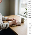 Person writing in journal at wooden desk by window 135220266
