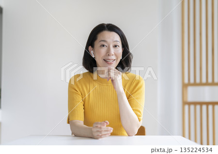 カメラ目線で話すイヤホンをつけた50代の女性 カメラ目線で話すイヤホンをつけた50代の女性 135224534