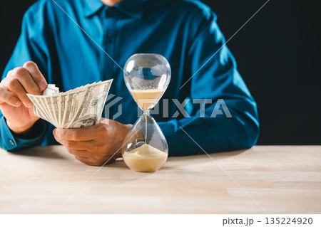 Person counts money banknotes, time sand hourglass flowing on table, illustrating business finance investment concepts, global wealth management, important saving for future 135224920