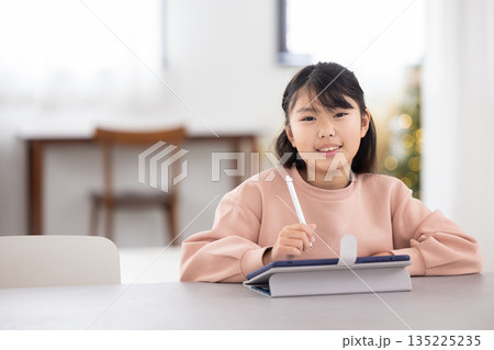 タブレットで勉強しながら微笑む小学生の女の子 タブレットで勉強しながら微笑む小学生の女の子 135225235