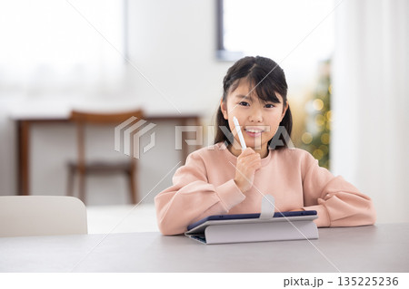 タブレットで勉強しながら微笑む小学生の女の子 タブレットで勉強しながら微笑む小学生の女の子 135225236