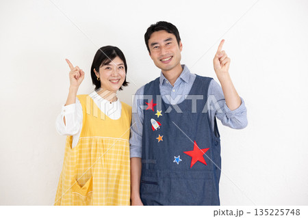 人差し指を立てて笑顔で微笑むエプロンを着た笑顔の男性保育士と女性保育士 135225748
