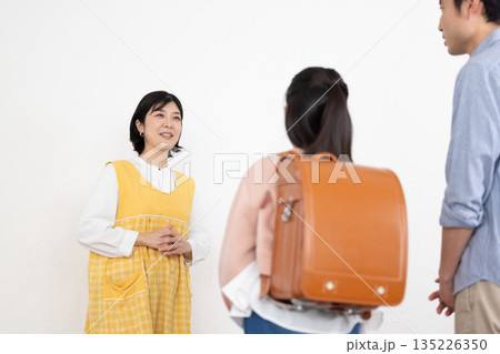 ランドセルを背負った小学生に微笑みかける学童の女性スタッフ 135226350