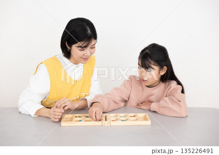 マンカラを楽しむ小学生の女の子とエプロンを着たミドル女性 135226491