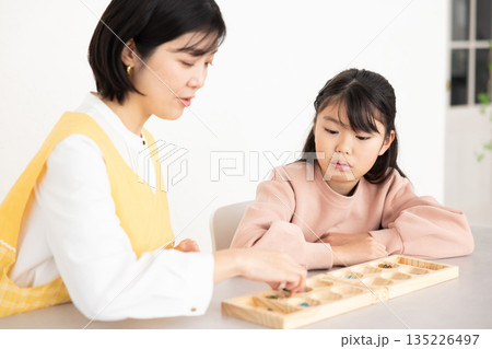 マンカラを楽しむ小学生の女の子とエプロンを着たミドル女性 マンカラを楽しむ小学生の女の子とエプロンを着たミドル女性 135226497