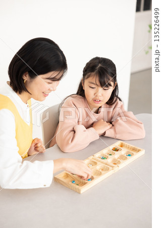 マンカラを楽しむ小学生の女の子とエプロンを着たミドル女性 135226499