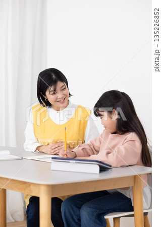 女子児童に勉強を教える学童指導員の女性 135226852